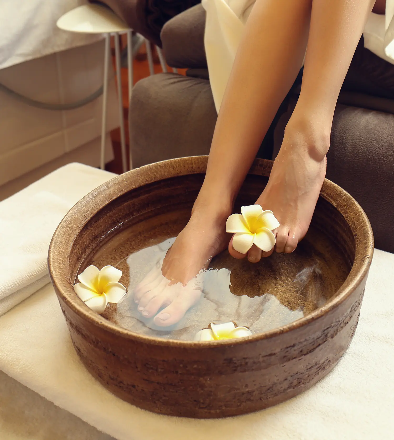 Woman soaking her feet in a bowl of water with flowers during her Blissful Feet Journey treatment at Pause Spa