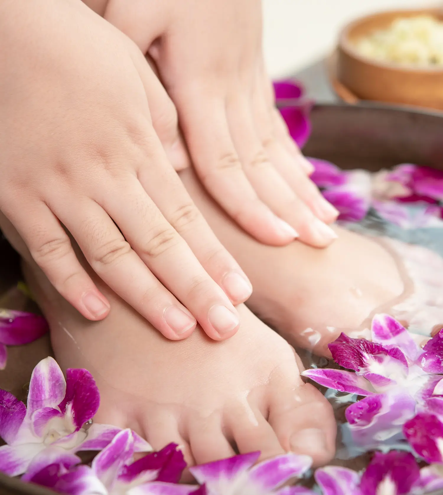 Woman's hands and feet in a bowl of water with flowers during her Hand or Foot Ritual treatment at Pause Spa